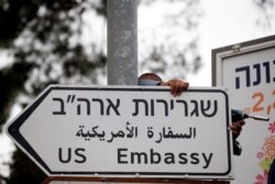 FILE - A worker hangs a road sign directing traffic to the U.S. Embassy, in the area of the U.S. Consulate, in Jerusalem, May 7, 2018.