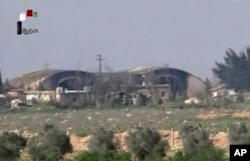 FILE - This frame grab from video provided April, 7, 2017, by official Syrian TV shows the burned and damaged hangars hit by U.S. Tomahawk missiles at the Shayrat air base southeast of Homs, Syria.