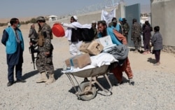 A worker from UNHCR pushes a wheelbarrow loaded with aid supplies for a displaced Afghan family outside the distribution center as a Taliban fighter secures the area on the outskirts of Kabul, Afghanistan, Oct. 28, 2021.
