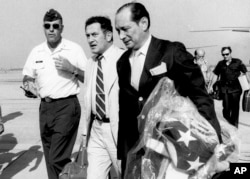 In this April 12, 1975, file photo, U.S. Ambassador to Cambodia John Gunther Dean carries the American flag from the U.S. Embassy in Cambodia as he arrives at Utapao Air Force Base in Thailand following the evacuation from Phnom Penh.