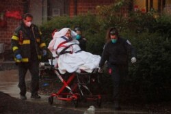Medics and firefighters bring a patient to the ambulance in the rain amid the coronavirus disease (COVID-19) outbreak at the West Revere Health Center in Revere, Massachusetts, April 21, 2020.