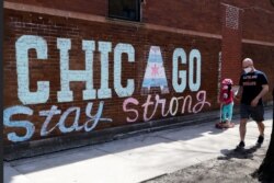 FILE - A man and child wearing protective masks pass an encouraging message "Chicago Stay Strong," while people continue to contract COVID-19 in Chicago, April 11, 2020.