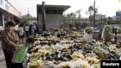 People stand next to flowers placed at an entrance to a subway station of Metro Line 5 in memory of flood victims following heavy rainfall in Zhengzhou, Henan province, on July 27, 2021. (Source: China Daily via Reuters) 