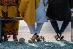 Commuters sit at a bus stop surrounded by broken glass in Dakar, Senegal Monday, March 8, 202, after violent protests erupted across the country. (Annika Hammerschlag/VOA)