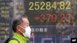 FILE - A man walks by an electronic stock board of a securities firm in Tokyo, November 11, 2020. 