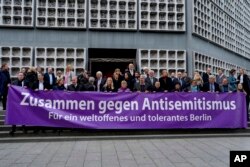 Warga dan politisi membentangkan spanduk bertuliskan "bersama melawan antisemitisme, demi Berlin yang berpikiran terbuka dan toleran" di luar gereja peringatan Kaiser Wilhelm di Berlin, Jerman, 7 Oktober 2024, menandai satu tahun serangan 7 Oktober 2023.(Markus Schreiber/AP)