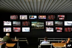 Men watch horse racing on an array of screen at Monmouth Park Racetrack in Oceanport, N.J., Monday, May 14, 2018.