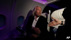 FILE - Virgin Group Founder Richard Branson greets a reporter as he sits in a Virgin America aircraft replica at an opening for a new cabin trainer facility at Virgin America corporate headquarters in Burlingame, California, Oct. 18, 2011.