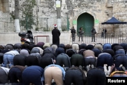 Palestinians pray as Israeli border police stand guard near the entrance door leading to the compound housing Al-Aqsa Mosque in Jerusalem's Old City, March 12, 2019.