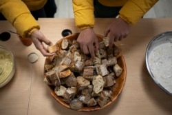 Migrants serve themselves bread during dinner offered at a migrant refuge in Briancon, France, Friday, Dec. 10, 2021.