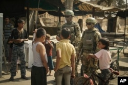 FILE - In this Sept. 15, 2017, photo, Russian soldiers escorting a group of journalists stand guard as children gather, in Deir ez-Zor, Syria.