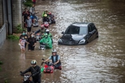Sejumlah pengendara motor berjalan sambil mendorong motor melalui jalan yang terendam banjir setelah hujan lebat mengguyur Jakarta, Sabtu, 20 Februari 2021. (Foto: Aprilio Akbar/Antara via Reuters)