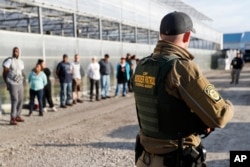 Government agents stand guard alongside suspects taken into custody during an immigration sting at Corso's Flower and Garden Center, June 5, 2018, in Castalia, Ohio.