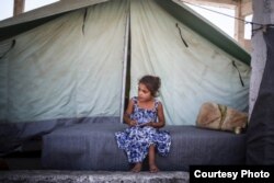 Silva, 7, writes in a notebook in front of her family’s tent at the Alexandria refugee camp in northern Greece. (Photo: courtesy: Tara Todras-Whitehill/IRC)