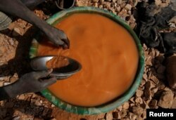 An artisanal miner pans for gold using a plastic wash basin and metal pan at an unlicensed mine near the city of Doropo, Ivory Coast, Feb. 13, 2018.