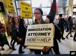 A woman offers legal services at the customs arrival area as demonstrators opposed to President Donald Trump's executive orders barring entry to the U.S. by Muslims from certain countries march behind at the Tom Bradley International Terminal at Los Angel