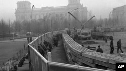 This Nov. 20, 1961 photo shows 12 feet high boards hiding the work as East German troops erect a new concrete wall at the Brandenburg Gate, marking the East-West border in Berlin. In background is the former Reichstag building which is in West Berlin. (A