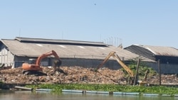 Dua eskavator memindahkan tumpukan sampah yang ada di pinggir sungai Surabaya wilayah Gunungsari, Surabaya, setelah terjaring pipa yang dipasang melintang di atas sungai (Foto: VOA/Petrus Riski)