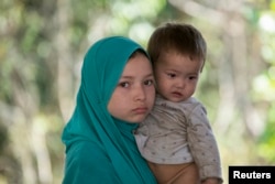 在泰国-马来西亚边界被拘留的一个疑似来自新疆的维吾尔人抱着一个孩子在临时收容所里（2014年3月14日）