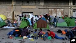 Refugees and migrants sit outside their tents at the Athens' port of Piraeus, March 10, 2016.