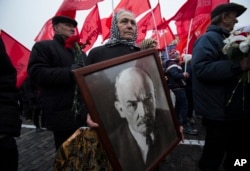 FILE - A woman carries a portrait of Lenin as she walks with the Communist Party members and supporters to place flowers at the Tomb of Soviet founder Vladimir Lenin, at Moscow's Red Square, Nov. 6, 2014.