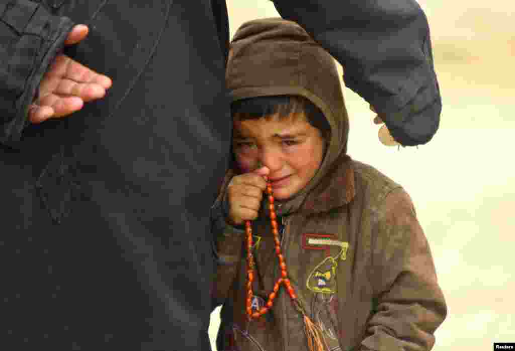 A boy, standing next to his father, cries as they wait to receive humanitarian aid in the countryside of Idlib January 13, 2013. 