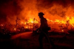 A firefighter hoses down areas of the Dixie Fire as it jumps Highway 395 south of Janesville, Calif., Aug. 16, 2021.