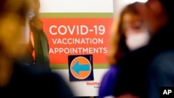 ស្លាកសញ្ញា​ដែល​មាន​សញ្ញា​ព្រួញ​បង្ហាញ​ទិសដៅ​នៅ​ខាងក្រោម បង្ហាញ​អំពី​កន្លែង​ដែល​ត្រូវ​ទៅ​ដើម្បី​ចុះ​​ឈ្មោះ​ណាត់​ពេល​ចាក់​វ៉ាក់សាំង​បង្ការ​ជំងឺកូវីដ​១៩ នៅឯ​មន្ទីរពេទ្យ Edward នៅ​ក្រុង Naperville រដ្ឋ Illinois នៅ​ថ្ងៃទី១៧ ខែធ្នូ ឆ្នាំ២០២០។