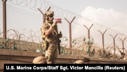 Seorang anggota pasukan koalisi memegang bendera Denmark untuk mengidentifikasi keluarganya saat evakuasi di bandara internasional Hamid Karzai, Kabul, Afghanistan, 21 Agustus 2021. (U.S. Marine Corps/Staff Sgt. Victor Mancilla/Handout via REUTERS)