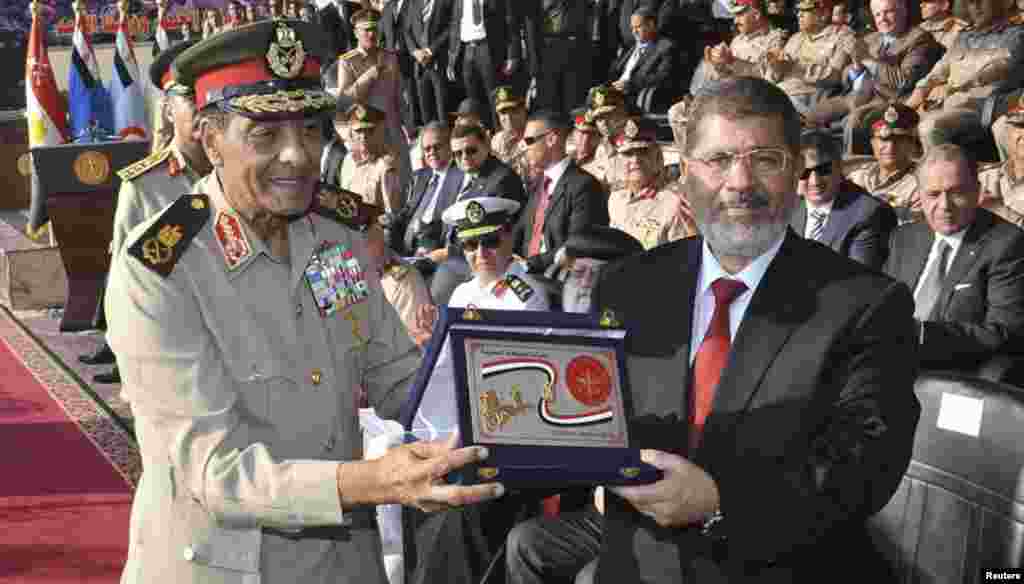 Egypt's new President Mohamed Morsi (R) poses with a gift from Field Marshal Mohamed Tantawi (L), head of Egypt's ruling Supreme Council of the Armed Forces (SCAF), during a ceremony where the military handed over power to Morsi at a military base in Hiks
