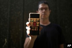 Yuval Haran, whose family is celebrating the return of his mother, his sister and four others from Hamas captivity in Gaza, poses for a portrait with a picture on his phone of his family's hostage posters, in Herziliya, Israel, on Dec. 4, 2023.