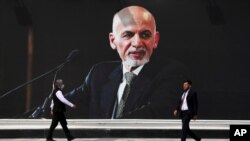 People walk near a mural of President Ashraf Ghani at Hamid Karzai International Airport, in Kabul, Afghanistan, Aug. 14, 2021.