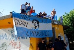 Fans stand on a roof of a house along the route of the motorcade carrying the remains of football star Diego Maradona to the Jardin de Bellavista cemetery in Buenos Aires, Argentina, Nov. 26, 2020.