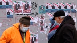 Pedestrians walk past a board bearing electoral campaign posters along a street in Abuzar, south of Tehran on Feb. 26, 2024, ahead of March 1 elections. Voters will pick new members of Iran's parliament, as well as the Assembly of Experts