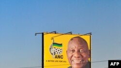 Afisa wa polisi wa Afrika Kusini akiendesha baiskeli kupita bango la matangazo ya Rais wa Afrika Kusini na mgombea wa chama tawala cha African National Congress (ANC) Cyril Ramaphosa kando ya Barabara ya Nelson Mandela katika kitongoji cha Seshego, karibu na Polokwane.