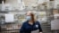 FILE- Cages loaded with ballots in U.S. Postal Service bins rest behind a worker at a Board of Elections facility in New York, July, 22, 2020. 