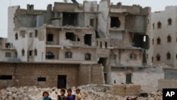 Dalam foto yang diambil pada tanggal 29 Mei 2018 ini, tampak anak-anak berjalan di depan gedung-gedung yang rusak perang di pinggiran al-Bab, Suriah utara. (Foto: AP/Lefteris Pitarakis)