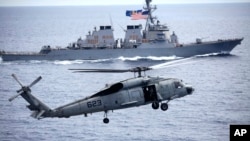 a U.S. Navy SH-60 Seahawk helicopter approaches to land on the deck of U.S. aircraft carrier, USS George Washington (CVN-73) with the backdrop of U.S. navy destroyer USS John S. McCain (DDG-56).