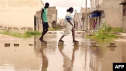 Des habitants marchent sur des briques placées dans des eaux inondées dans le quartier de Keurs Massar à Dakar le 7 septembre 2020 après de fortes pluies au Sénégal.