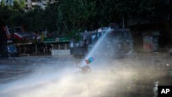 An anti-government protester, holding a Mapuche flag, is brought down by the jet spray of a police water cannon, in Santiago, Chile, Oct. 31, 2019.