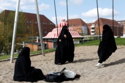 FILE - Young Muslim women in burqas chat on a playground in a park near Mjolnerparken, in Copenhagen, Denmark, May 3, 2018.