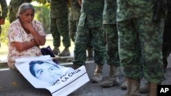 FILE - The mother of missing college student Adan Abarajan de la Cruz sits at the foot of soldiers outside a military base during a protest by the families of 43 missing students over the army's alleged responsibility or lack of response to the students' disappearance in Iguala, Mexico, Dec. 18, 2014. 