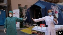 Monica Carfora, right, deputy head of the emergency of the Santo Spirito Hospital poses for a photograph with nurse Silvia Sforza, holding out their arms to indicating social distancing in Rome, April, 12, 2020. 