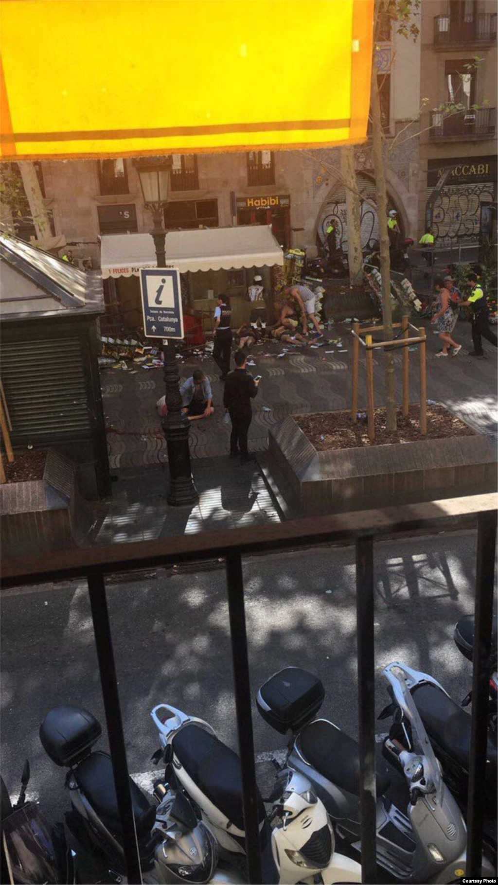 Police officers and bystanders are seen assisting injured people on the ground after a van plowed through a sidewalk, at Las Ramblas, near Placa de Catalunya, in Barcelona, Spain, Aug. 17, 2017. (Courtesy - Jordi Ramos)