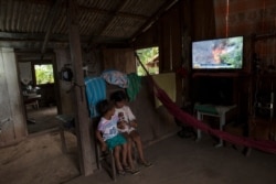 Children play with a cell phone as a television news airs in the background in the Cajueiro village, Para state, Brazil, Sept. 3, 2019.