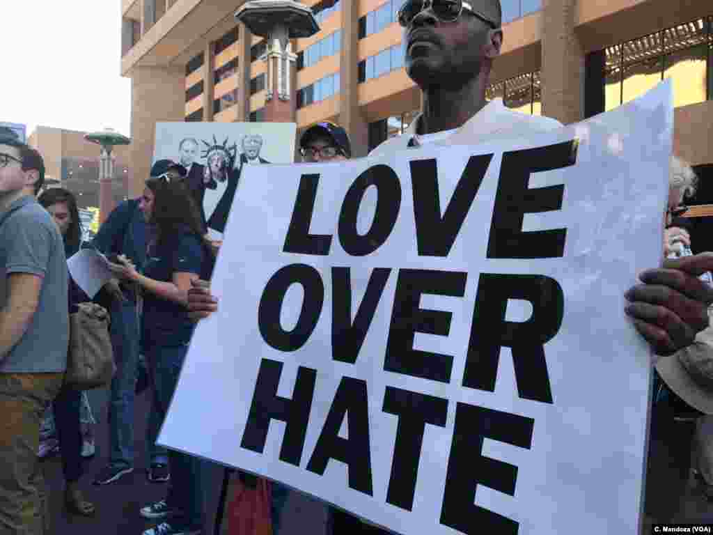 A man stands in silence with his sign protesting President Donald Trump, who was to give a campaign-style rally in Phoenix, Aug. 22, 2017. He is facing Trump supporters using a bullhorn to shout their message.
