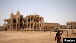 FILE - A man carries a table as he walks past the ruins of a building in the port city of Massawa, Eritrea, July 22, 2018. 