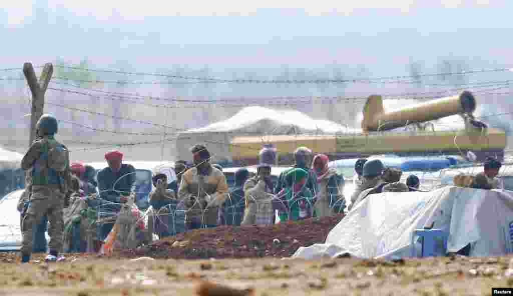 A Turkish soldier stands guard as Syrian Kurdish refugees wait behind the border fences to cross into Turkey near the southeastern town of Suruc in Sanliurfa province, Turkey, Oct. 17, 2014.