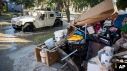 FILE - A military vehicle passes flood-damaged belongings piled on a homeowners' front lawn in the aftermath of Hurricane Harvey at the Canyon Gate community in Katy, Texas, Sept. 7, 2017.