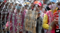 Cambodian garment workers shout slogans behind barbed wire set up by police near the Council of Ministers building during a rally in Phnom Penh, Cambodia, Monday, Dec. 30, 2013. The workers are demanding a raise in their monthly salary from US $160 to $80. (AP Photo/Heng Sinith)